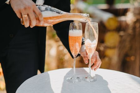 Man's hand pouring champagne into wine glasses on the table. Closeup.の写真素材