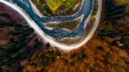 Beautiful view from a drone above river, road and autumn forest with green spruces and trees with colorful red foliage in the Carpathian mountains.の写真素材