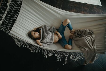 Young pregnant woman in pullover and jeans lies and sleeps in hammock. Top view.の写真素材