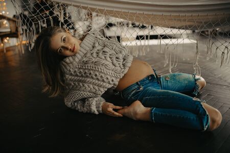 Young pregnant woman in pullover and jeans sits at the floor next to hammock.の写真素材