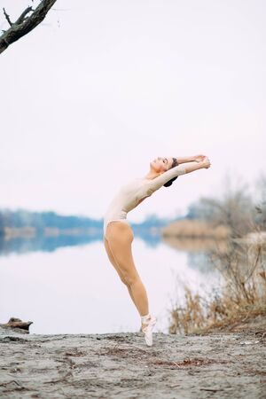 Ballerina dances at the lake shore on the background of water and sky.の写真素材