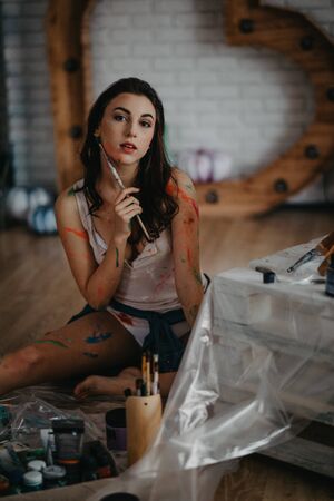 The artist stained with paint sits in an art workshop and ponders about her picture.の写真素材