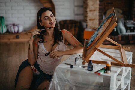 The artist stained with paint sits on floor in an art workshop in a creative mess.の写真素材