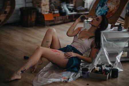 The artist stained with paint sits on floor in an art workshop in a creative mess.の写真素材