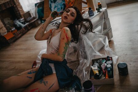 The artist stained with paint sits on floor in an art workshop in a creative mess.の写真素材