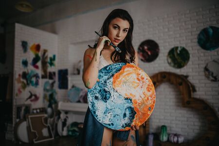 The artist stained with paint stands in an art workshop with het picture in her hands.の写真素材