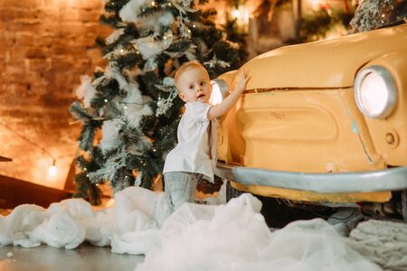 Little boy stands next to retro car against background of Christmas tree and decorations.の写真素材