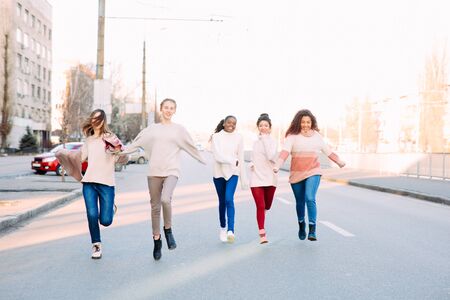 Multiracial group of friends from five young women runs and has a fun on city street. The concept of friendship and unity between different human races.の写真素材