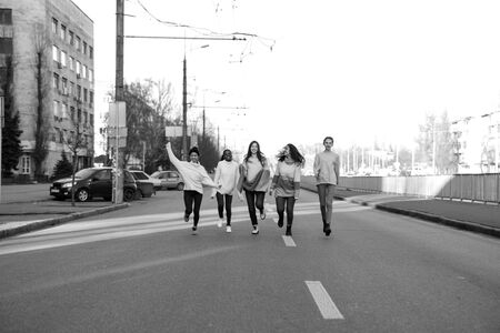 Multiracial group of friends from five young women runs and has a fun on city street. The concept of friendship and unity between different human races. Black and white image.の写真素材