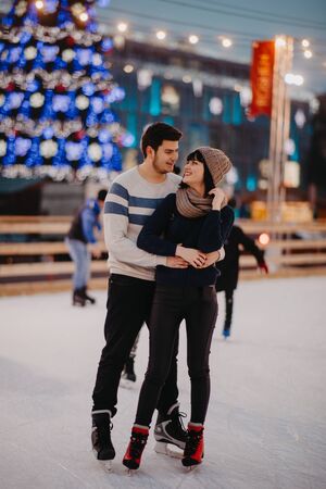 Young couple skates at the rink on the background of Christmac tree and decorations.の写真素材