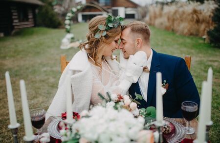 Newlyweds sit near banquet table and embrace on background of lawn.の写真素材