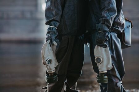 Couple in love stands under bridge in  protective suits and gas masks in their hands. Concept of a preventive measures and protection for coronavirus COVID 19 pandemic and other global dangers.の写真素材
