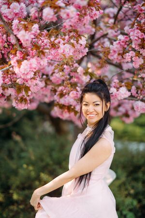 Young woman in white dress and hat has enjoy and relaxes in park with blooming sakura trees.
