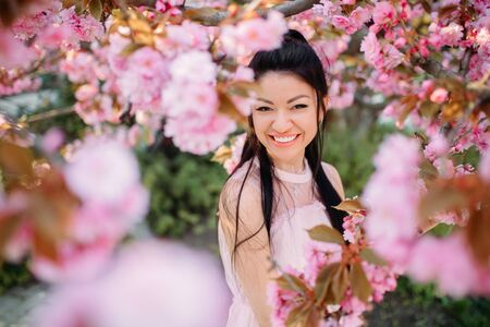 Young woman in white dress has enjoy and relaxes in park with blooming sakura trees. Portrait.の写真素材