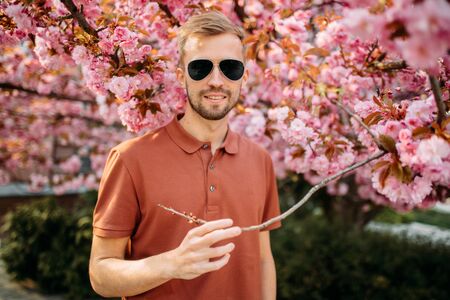 Portrait of young man in sunglasses who enjoys and relaxes in park with blooming sakura trees.の写真素材
