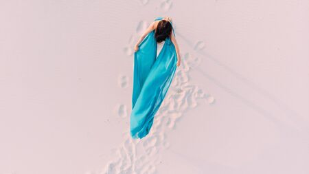 Woman wrapped in blue tissue posing in the desert on sand