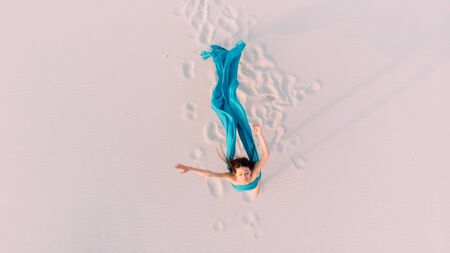 Woman wrapped in blue tissue posing in the desert on sandの写真素材