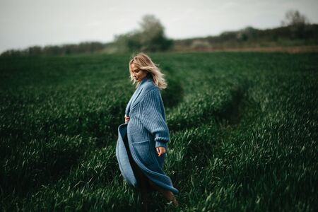 A young woman in blue jacket walks among the green field of wheat.の写真素材