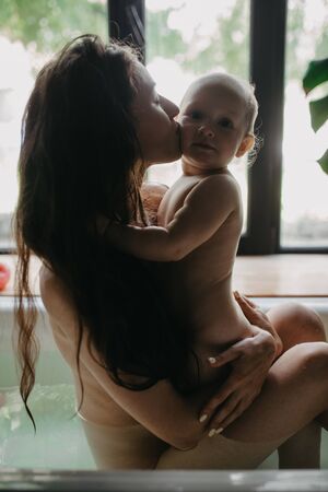 Mother hugs and kisses her baby while bathing in bathtub. Closeup.の写真素材
