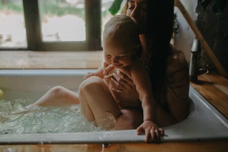 Mother hugs her baby while bathing in bathtub. Closeup.の写真素材