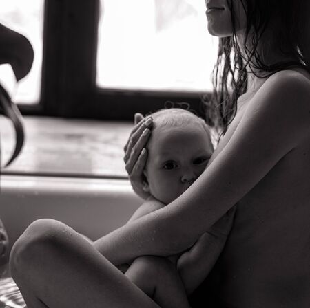 Mother bathes in bathtub and breastfeeds her baby. Closeup. Black and white image.の写真素材