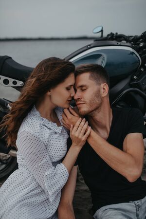 Couple in love sits and hugs on sandy beach near motorcycle.の写真素材