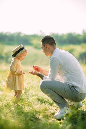 A father gives his daughter berries during a walk in the meadow.の写真素材