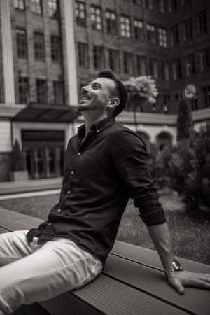 Young man sits and laughs on bench. Black and white image.