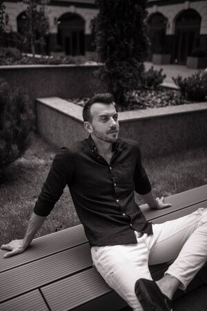 Young man sits and ponders on bench. Black and white image.