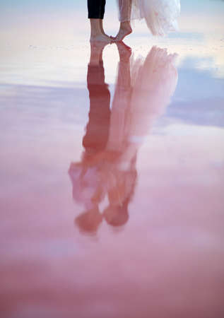 Barefoot legs of newlyweds are on the pink salty Genichesk lake in Ukraine. Closeup.