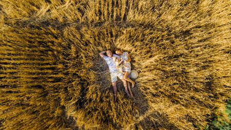 View from drone to happy young family lying and resting among yellow wheat field with baby.の写真素材