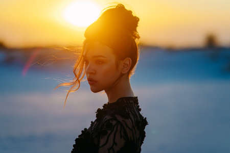 Woman in lace black dress stands in desert on background of sandy landscape at sunset. Portrait.