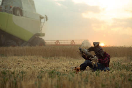 Man in image of sorcerer in hat with rabbit ears sits near doll among wheat field and performs a...