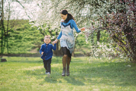 Happy mother and son run and have a fun on sunlit glade against background of blooming spring garden.の写真素材