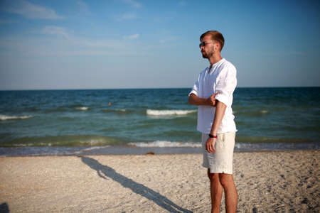 Young man in sunglasses stands on beach against sea and sky background. Copy space.の写真素材