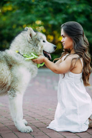 Young woman with innate disorder dwarfism embraces Malamute dog while walking in park.