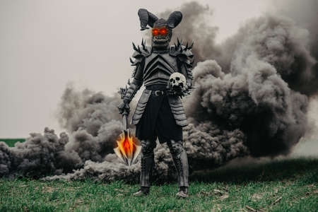 Mutant warrior stands with glowing eyes and holds mace and a human skull in his hands against a...