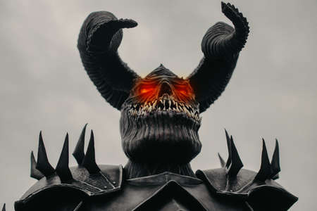 Portrait of a mutant warrior in armor with terrible teeth, horns and glowing eyes against sky background.の写真素材