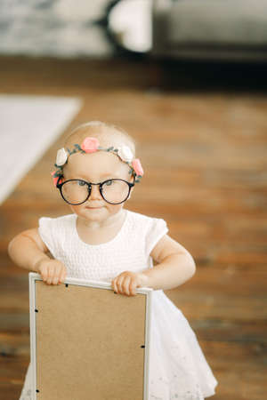 Baby girl stands in glasses and wreath in her head and holds picture.の写真素材