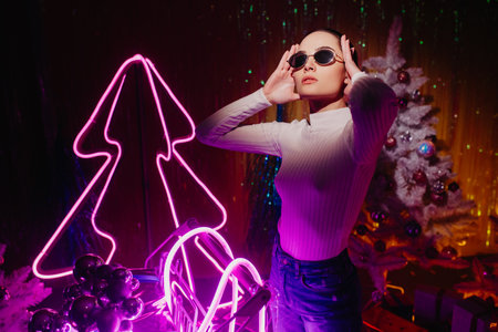 Young woman stands near supermarket trolley against background of Christmas tree and illumination.の写真素材