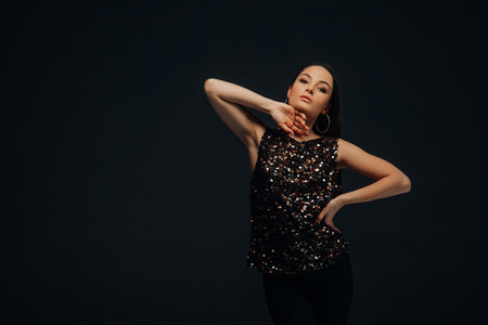 Young woman poses in shiny blouse and black pants against of black background. Image with copy...