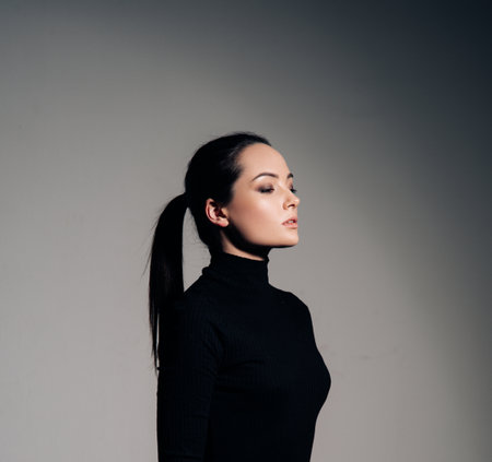 Portrait of young woman in black turtleneck with hairstyle tail against of gray background. Side view.の写真素材