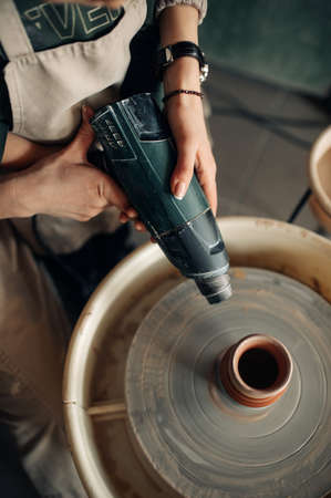 Expert potter assists child to dry earthenware cup on pottery wheel using dryer tool.の写真素材
