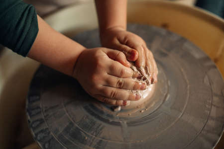 Child hands make earthenware cup working on pottery wheel at workshop. Top view. Closeup.の写真素材
