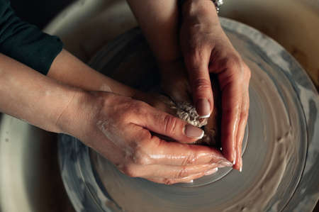 Expert potter assists child hands to make earthenware cup on pottery wheel.の写真素材