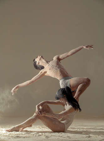 Two ballet dancers perform dance on the floor covered flour against background of white flour cloud in air.の写真素材