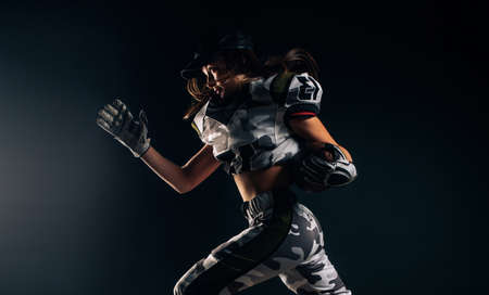 Beautiful sexy athletic woman runs on black background in American football uniform and cap with ball in her hands.の写真素材