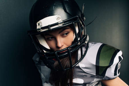 Portrait of beautiful sexy young woman on black background in American football uniform and helmet.の写真素材