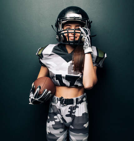 Portrait of beautiful sexy smiling woman on black background in American football uniform and helmet.の写真素材