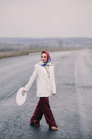 Young elegant woman walks on highway in countryside dressing in pants, jacket and shawl.の写真素材